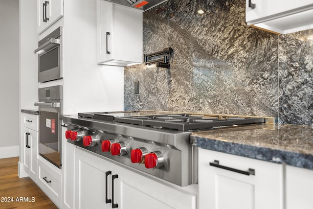 kitchen with backsplash, stainless steel gas stovetop, white cabinetry, dark stone countertops, and dark wood-type flooring