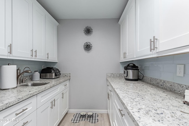 kitchen with baseboards, light wood finished floors, a sink, white cabinets, and tasteful backsplash