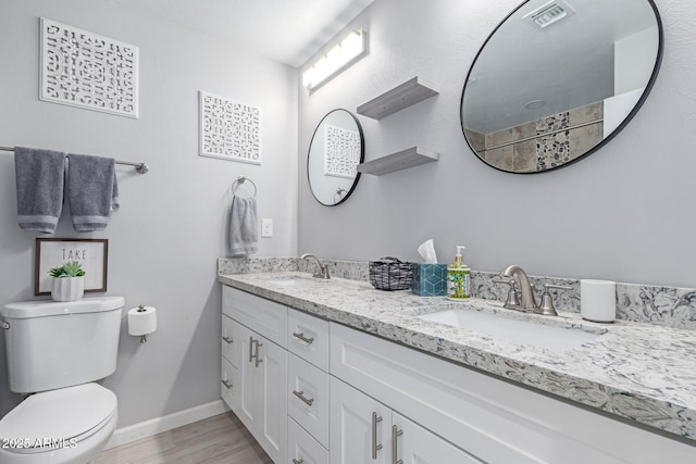 bathroom with toilet, wood finished floors, baseboards, and a sink