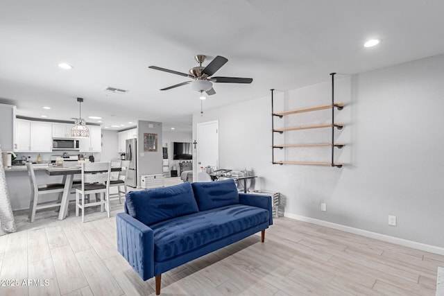 living room featuring ceiling fan, baseboards, visible vents, and light wood-type flooring