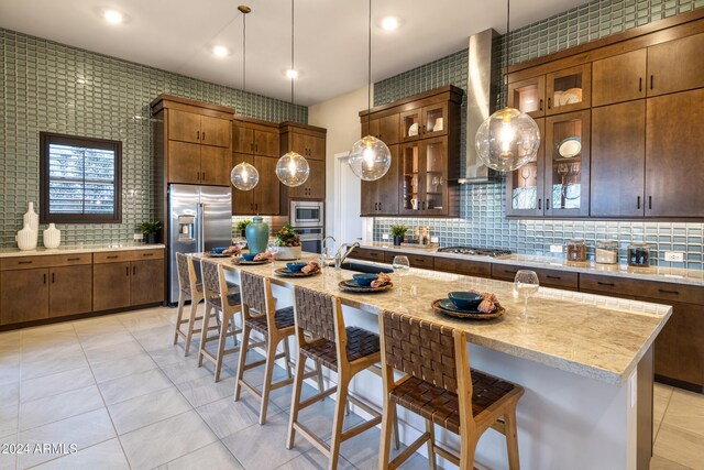 kitchen with stainless steel appliances, decorative backsplash, wall chimney exhaust hood, a center island with sink, and a breakfast bar