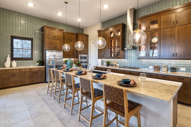 kitchen featuring built in appliances, a breakfast bar, an island with sink, glass insert cabinets, and pendant lighting