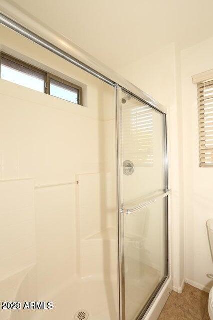 bathroom featuring toilet, a healthy amount of sunlight, and a shower with door