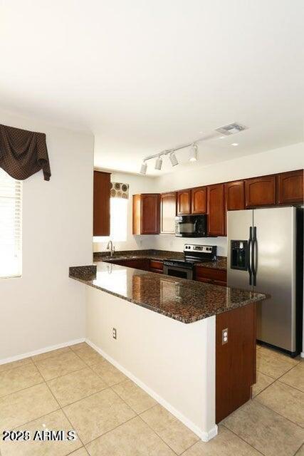 kitchen featuring kitchen peninsula, stainless steel appliances, dark stone counters, and light tile patterned flooring