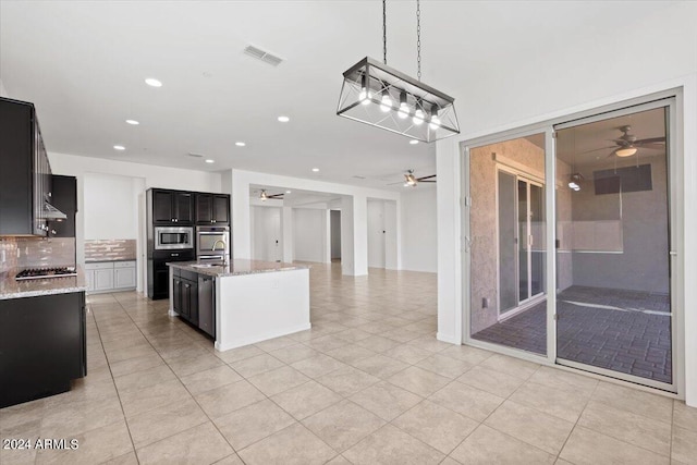 kitchen with sink, light stone counters, appliances with stainless steel finishes, tasteful backsplash, and a kitchen island with sink