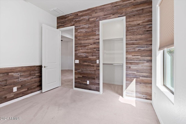 unfurnished bedroom with a walk in closet, wooden walls, and light carpet