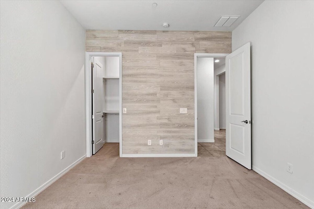 unfurnished bedroom featuring wood walls, a walk in closet, a closet, and carpet floors