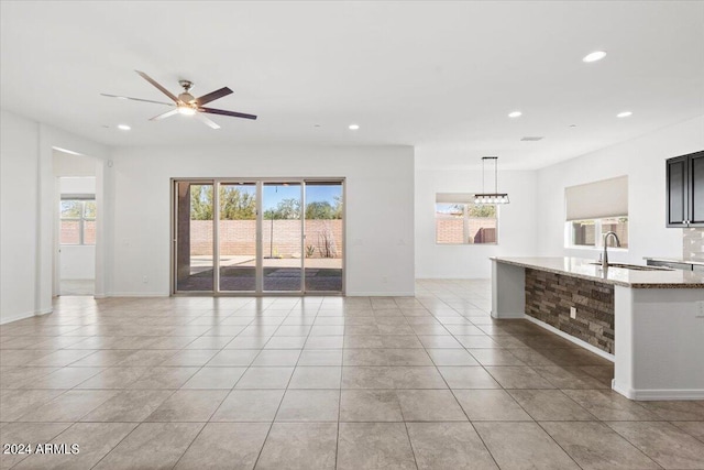 unfurnished living room featuring a wealth of natural light, ceiling fan, light tile patterned floors, and sink