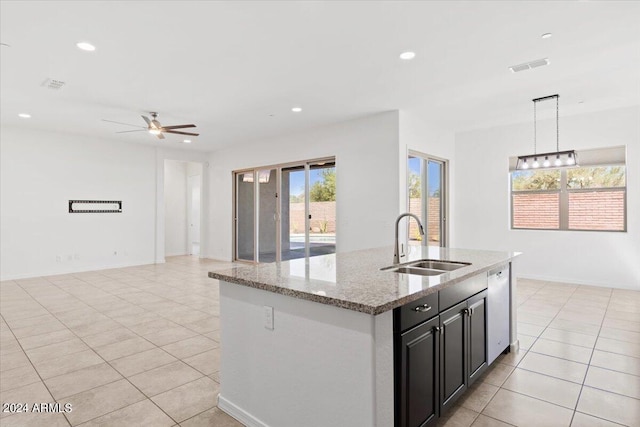 kitchen with light stone counters, dishwasher, sink, an island with sink, and decorative light fixtures