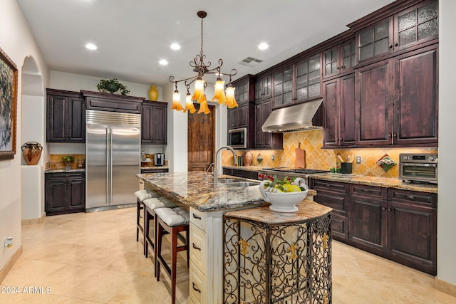 kitchen featuring sink, a kitchen island with sink, appliances with stainless steel finishes, a kitchen breakfast bar, and an inviting chandelier