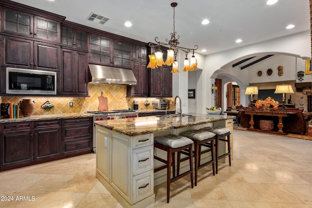 kitchen featuring an island with sink, black microwave, light stone countertops, sink, and a chandelier