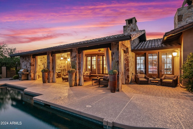 back house at dusk with a patio, outdoor lounge area, and french doors