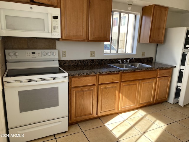 kitchen featuring dark stone countertops, white appliances, sink, and light tile patterned floors