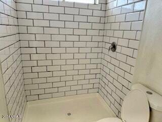 bathroom featuring tiled shower and toilet