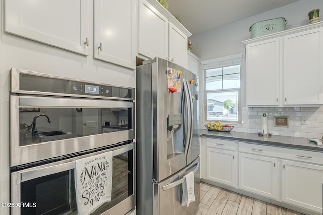 17253 W Echo Ln, Waddell, AZ 85355 - kitchen featuring stainless steel appliances, white cabinets, decorative backsplash, dark countertops, and light wood-style floors