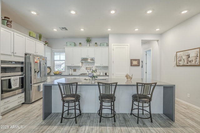 17253 W Echo Ln, Waddell, AZ 85355 - kitchen featuring stainless steel appliances, white cabinetry, light wood-style flooring, a kitchen breakfast bar, and recessed lighting
