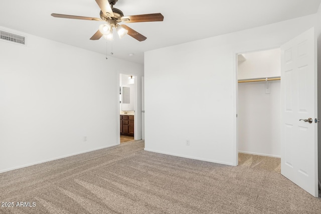 unfurnished bedroom featuring light carpet, connected bathroom, a spacious closet, and ceiling fan