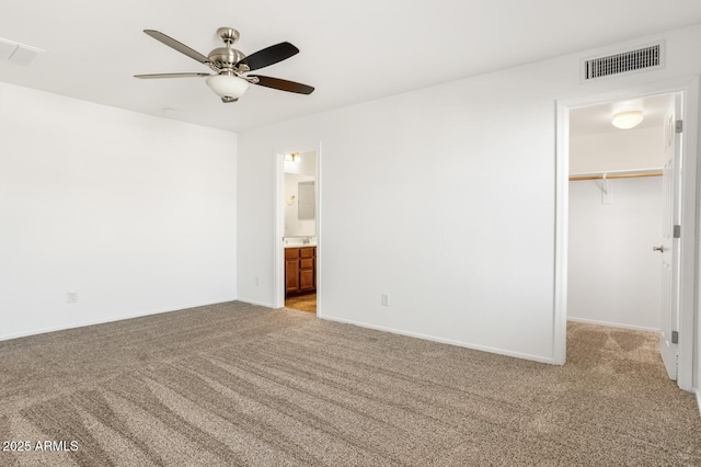 unfurnished bedroom featuring a walk in closet, ensuite bath, ceiling fan, light colored carpet, and a closet