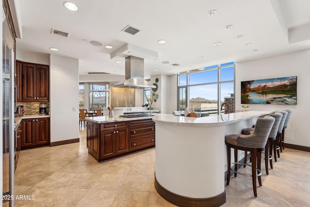 kitchen featuring island exhaust hood, decorative backsplash, recessed lighting, baseboards, and a breakfast bar area