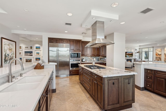 kitchen featuring built in appliances, a sink, island range hood, recessed lighting, and tasteful backsplash