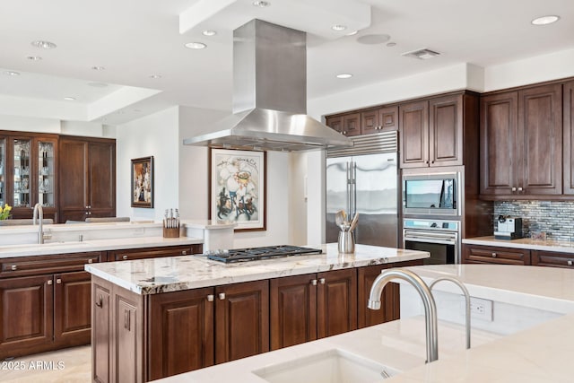 kitchen featuring island exhaust hood, a sink, built in appliances, recessed lighting, and decorative backsplash
