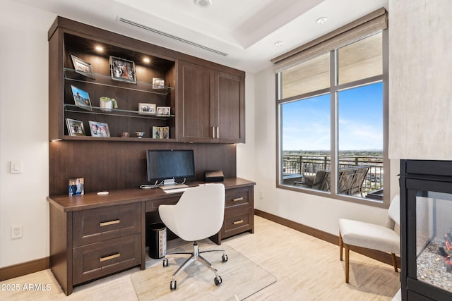 office area featuring baseboards, light wood-type flooring, and built in desk