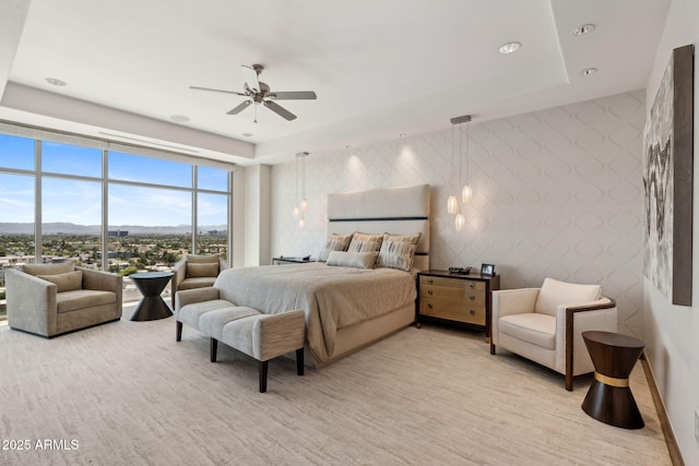 bedroom featuring a raised ceiling, a mountain view, a ceiling fan, and expansive windows