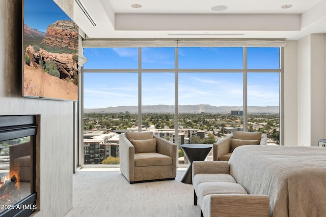 bedroom featuring floor to ceiling windows, a glass covered fireplace, a tray ceiling, and wood finished floors