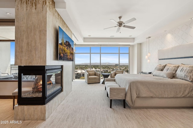 bedroom with a multi sided fireplace, expansive windows, wood finished floors, and a ceiling fan