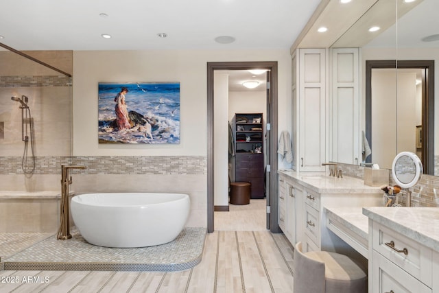 bathroom featuring vanity, wood finished floors, a freestanding bath, tile walls, and recessed lighting