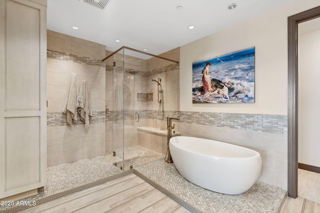 bathroom with tile walls, a freestanding bath, a shower stall, recessed lighting, and wood finished floors