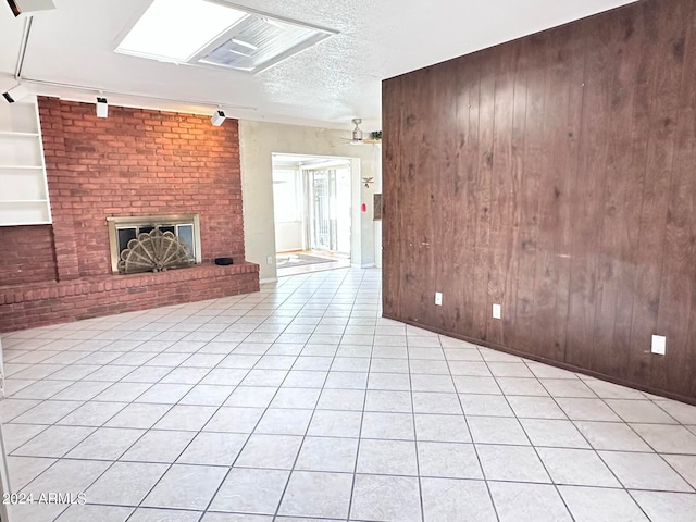 unfurnished living room with a brick fireplace, light tile patterned flooring, wood walls, and rail lighting