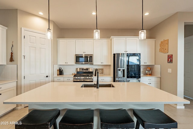 kitchen with stainless steel appliances, sink, white cabinets, backsplash, and a center island with sink