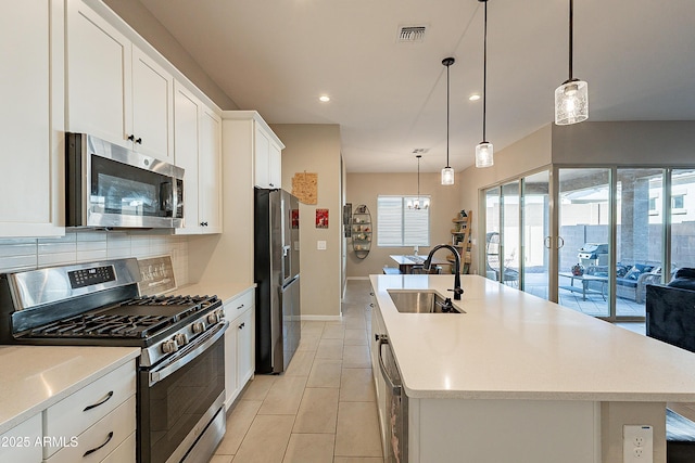 kitchen featuring stainless steel appliances, sink, white cabinets, a center island with sink, and pendant lighting