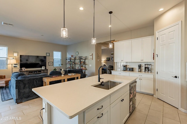 kitchen with white cabinets, decorative light fixtures, a kitchen island with sink, and sink