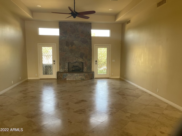 unfurnished living room featuring a fireplace, a high ceiling, a raised ceiling, and ceiling fan