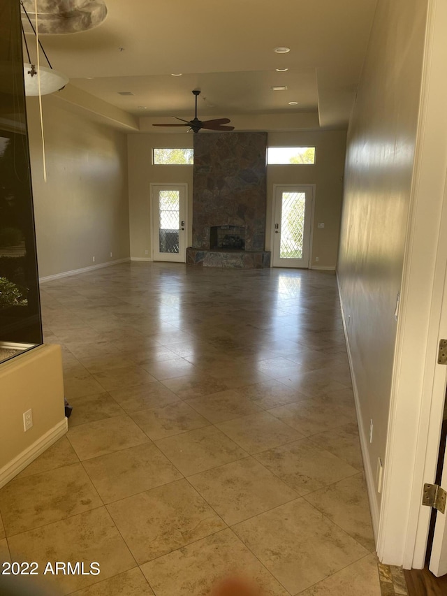 unfurnished living room with ceiling fan, a fireplace, a wealth of natural light, and a tray ceiling