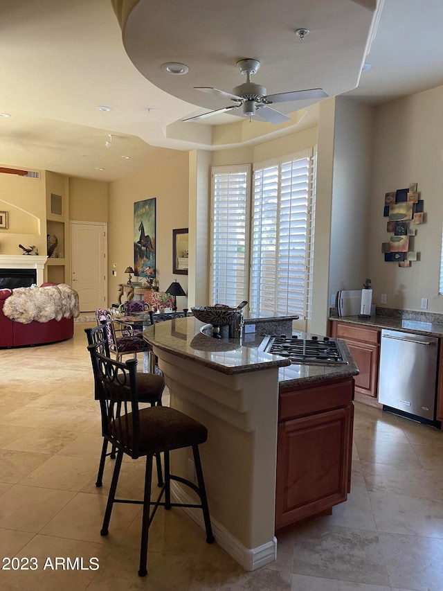 kitchen with a kitchen breakfast bar, dark stone counters, stainless steel appliances, ceiling fan, and a center island