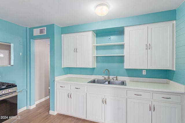 kitchen featuring gas range, white cabinetry, sink, and light hardwood / wood-style floors