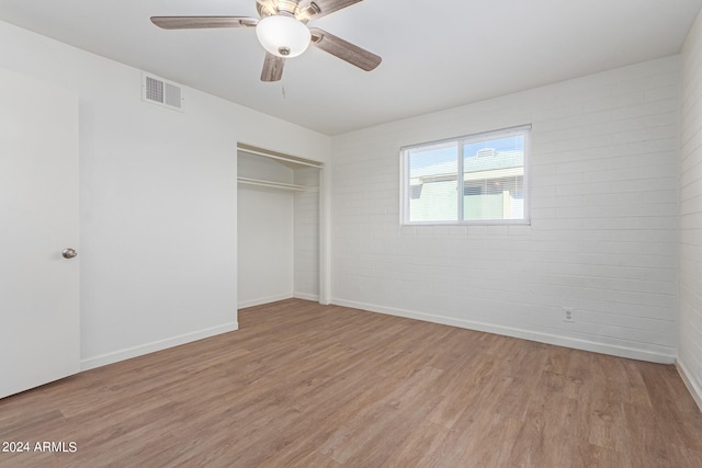 unfurnished bedroom with brick wall, light hardwood / wood-style flooring, a closet, and ceiling fan