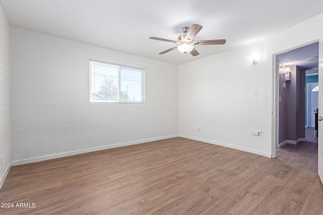 spare room featuring ceiling fan, hardwood / wood-style flooring, and brick wall