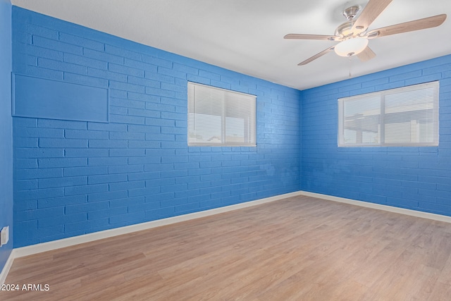 spare room featuring ceiling fan, brick wall, plenty of natural light, and light wood-type flooring