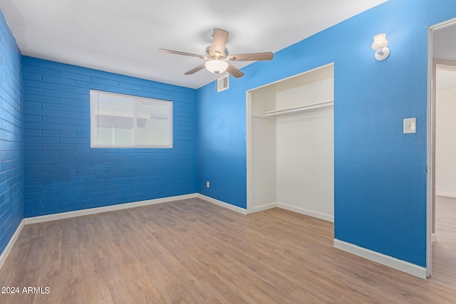 unfurnished bedroom featuring a closet, ceiling fan, brick wall, and light wood-type flooring