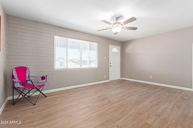 unfurnished room featuring brick wall, light wood-type flooring, and ceiling fan