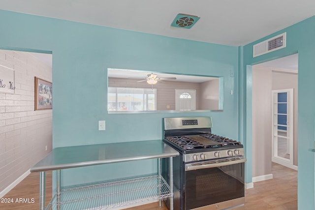 kitchen featuring stainless steel range with gas stovetop, ceiling fan, brick wall, and light hardwood / wood-style flooring