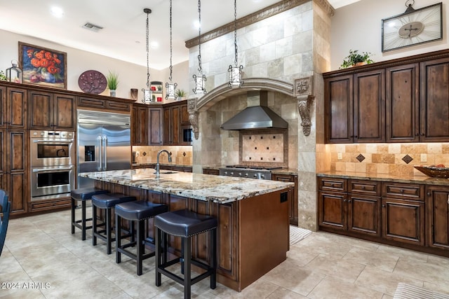 kitchen featuring wall chimney range hood, a kitchen bar, visible vents, light stone countertops, and stainless steel appliances