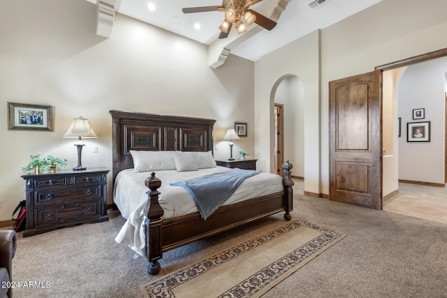 bedroom with ceiling fan, light colored carpet, arched walkways, baseboards, and a high ceiling