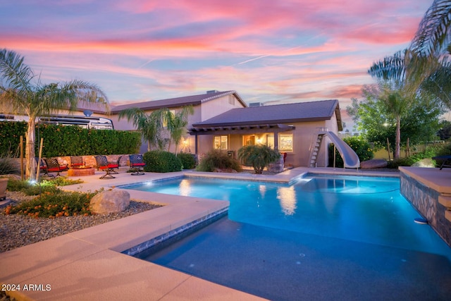 pool at dusk featuring a fenced in pool, a patio area, and a water slide