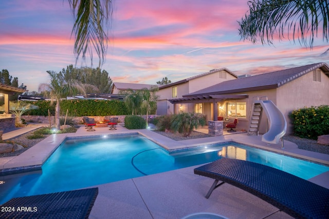 pool at dusk with a patio, a water slide, an outdoor hangout area, and a fenced in pool