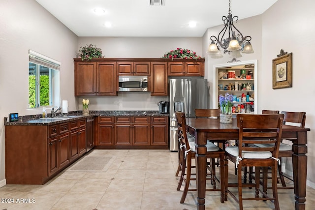 kitchen featuring appliances with stainless steel finishes, hanging light fixtures, a sink, light tile patterned floors, and dark stone counters